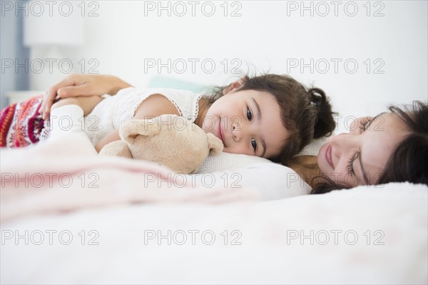 Hispanic mother and daughter relaxing on bed