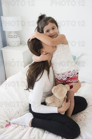 Hispanic mother and daughter relaxing on bed