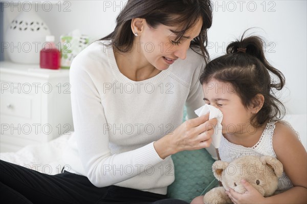 Hispanic mother wiping daughter's nose