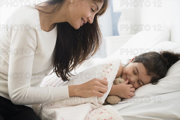 Hispanic mother tucking daughter into bed