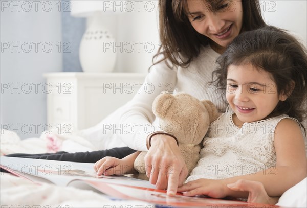 Hispanic mother and daughter reading in bed