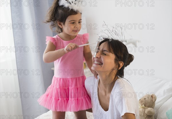 Hispanic mother and daughter playing dress up on bed