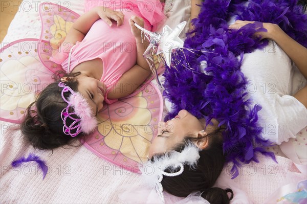 Hispanic mother and daughter playing dress up on bed