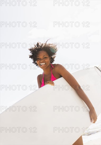 African American woman carrying surfboard on beach