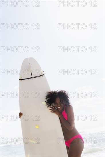 African American woman holding surfboard on beach