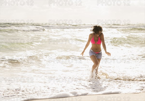 African American woman playing in waves on beach