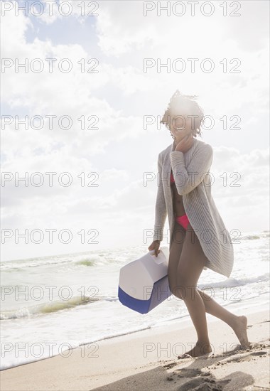 African American woman carrying cooler on beach