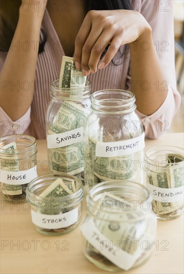 Mixed race woman putting money in savings jars