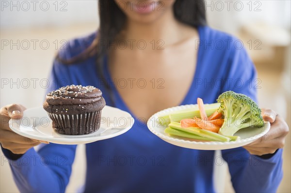 Mixed race woman choosing vegetables or cupcake