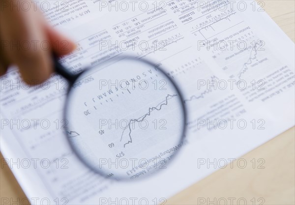Mixed race woman reading graph with magnifying glass