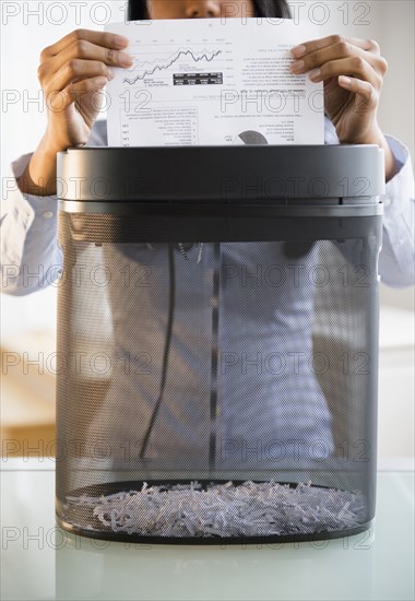 Mixed race businesswoman shredding documents