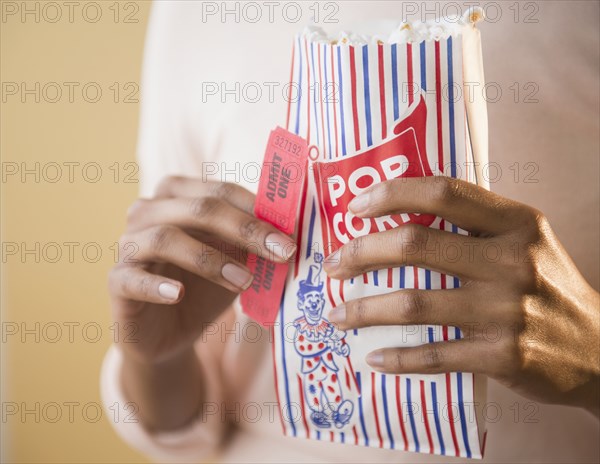 Mixed race woman with bag of popcorn and movie tickets