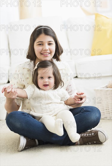 Hispanic girl holding toddler sister in living room