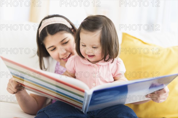 Hispanic girl reading to toddler sister in living room
