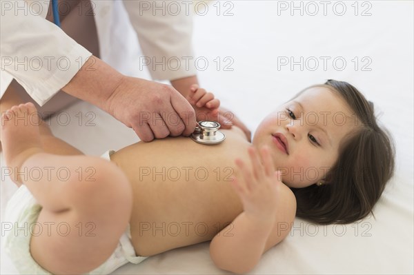 Hispanic doctor listening to toddler's heartbeat