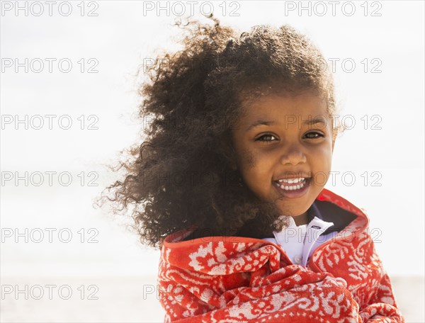 Mixed race girl wrapped in towel on beach