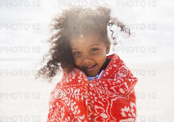 Mixed race girl wrapped in towel on beach