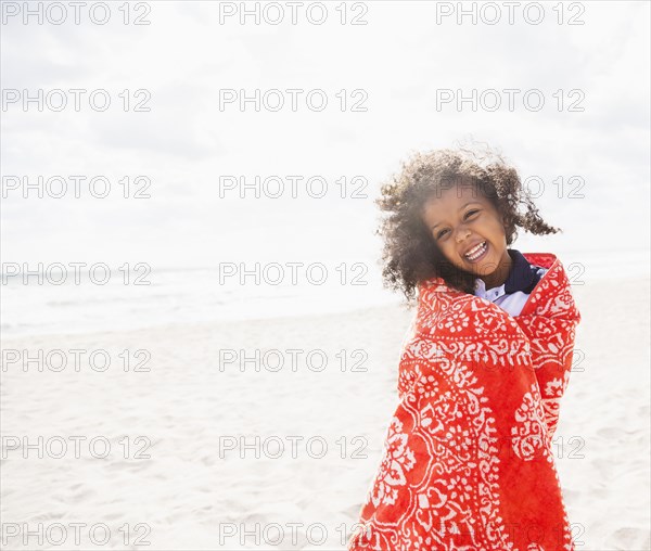Mixed race girl wrapped in towel on beach