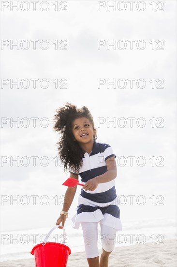 Mixed race girl carrying shovel and bucket on beach