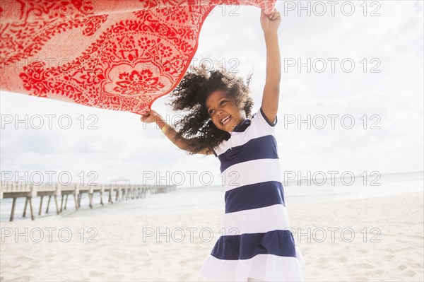 Mixed race girl playing with towel on beach