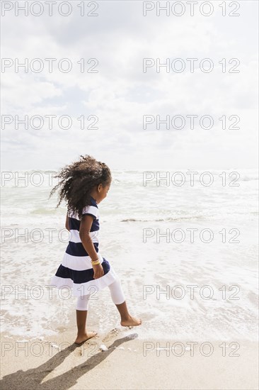 Mixed race girl walking in waves on beach