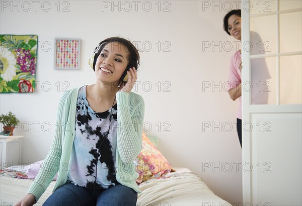 Mother checking on teenage girl listening to headphones