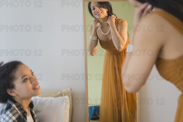 Teenage girl watching mother put on evening gown