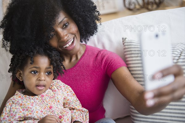 Mother taking photograph with daughter on sofa