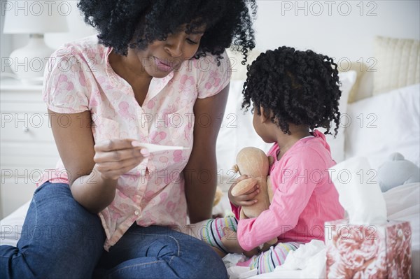 Mother checking daughter's temperature on bed