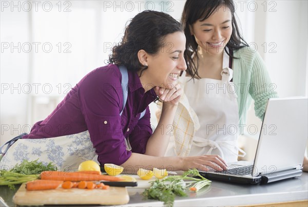 Women using laptop and cooking together