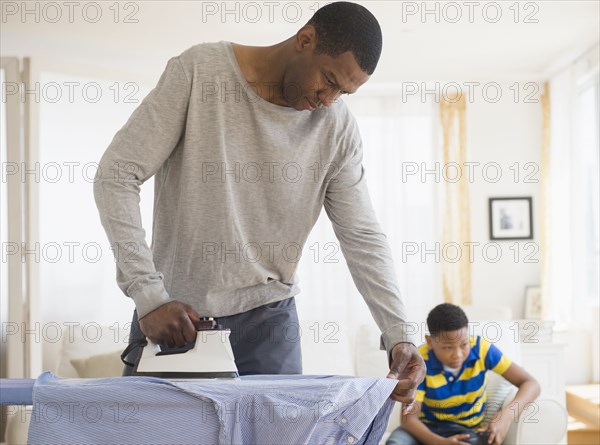 Father ironing shirt while son plays video games