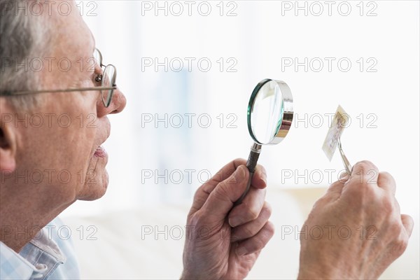 Senior Caucasian man examining stamp with magnifying glass