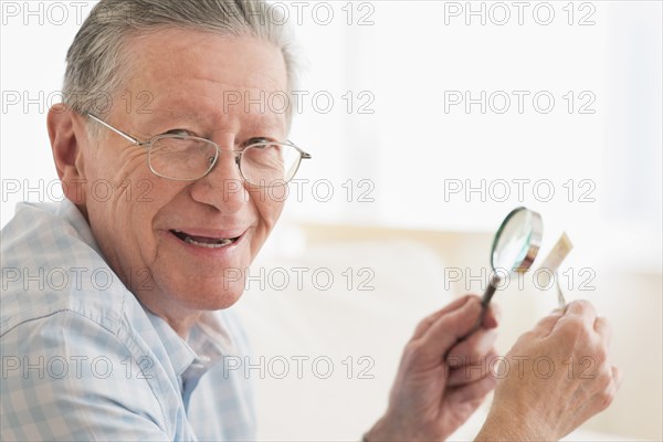 Senior Caucasian man examining stamp with magnifying glass