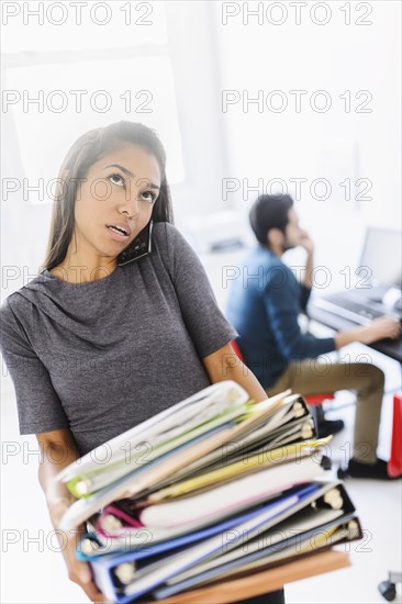 Hispanic businesswoman carrying stack of folders in office