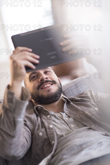 Hispanic man using digital tablet on sofa