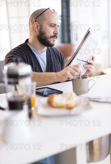 Hispanic man reading newspaper at breakfast