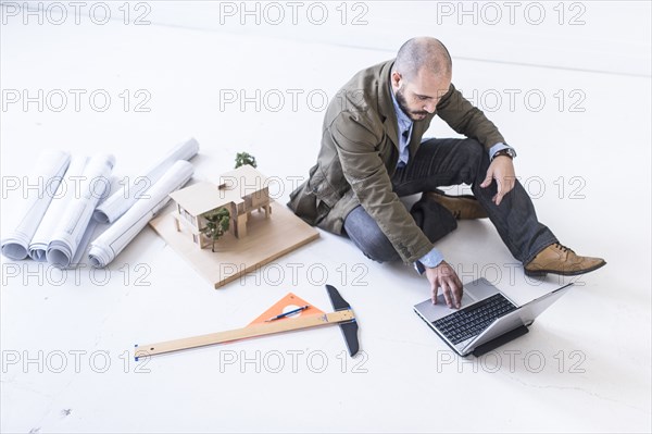 Hispanic architect using laptop on floor
