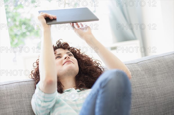 Hispanic woman using digital tablet on sofa