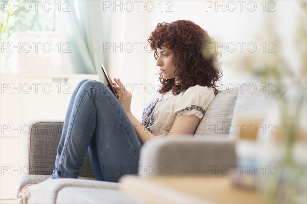 Hispanic woman using digital tablet on sofa