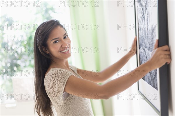 Hispanic woman hanging picture in living room