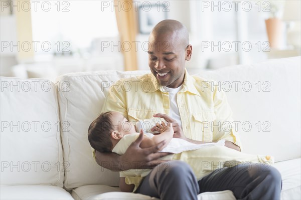 Smiling father feeding baby on sofa