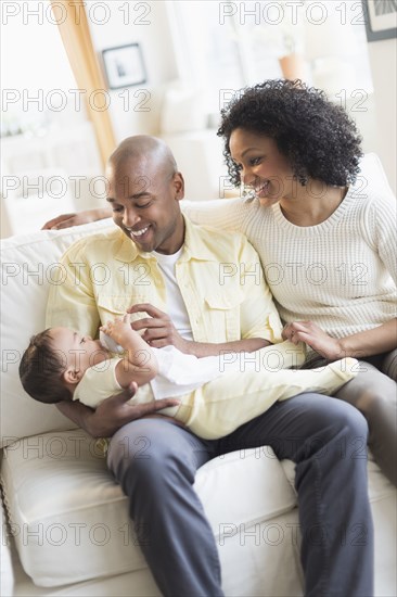 Smiling father feeding baby on sofa