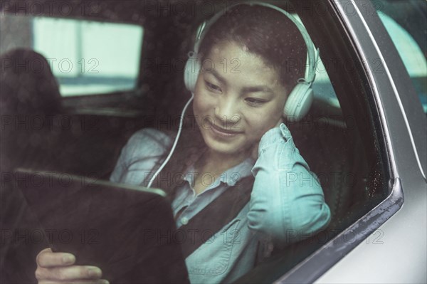 Mixed race teenage girl using digital tablet in backseat of car