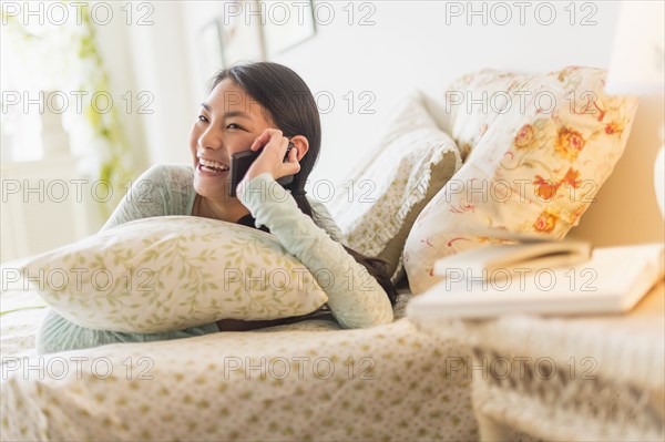 Mixed race teenage girl talking on cell phone on bed