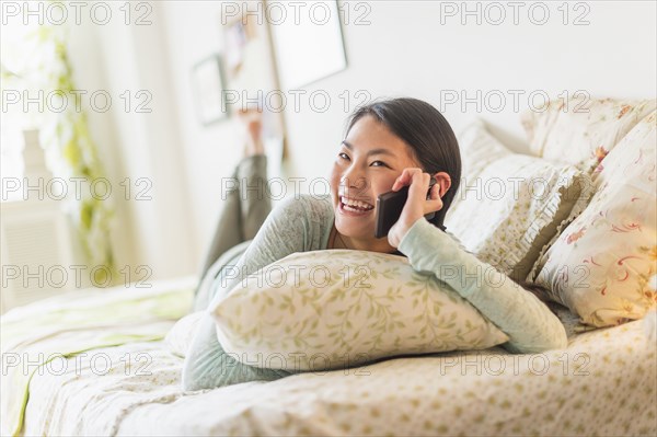 Mixed race teenage girl talking on cell phone on bed