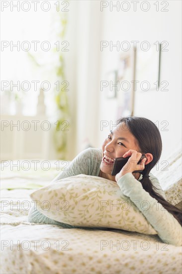 Mixed race teenage girl talking on cell phone on bed