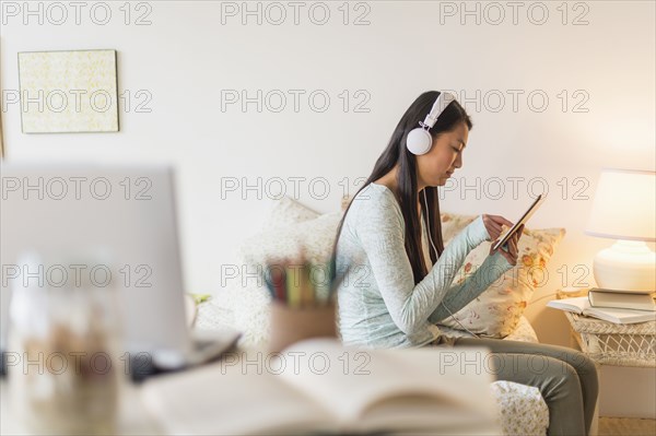 Mixed race teenage girl using digital tablet on bed