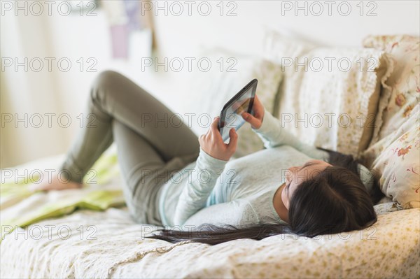 Mixed race teenage girl using digital tablet on bed