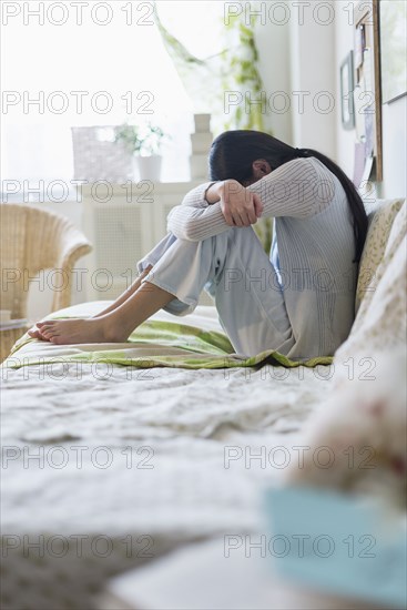 Mixed race teenage girl hugging her knees on bed