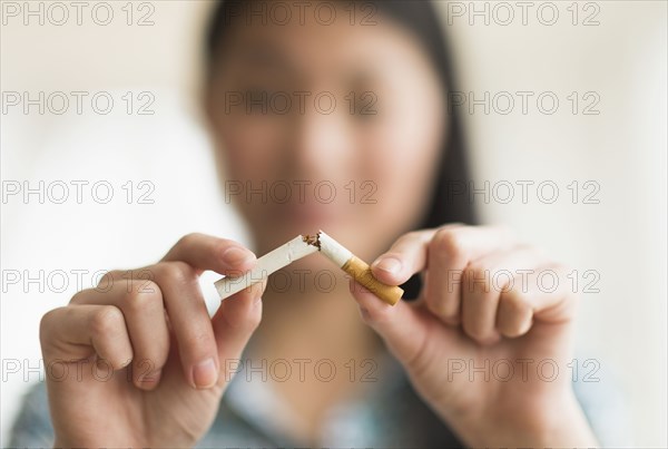 Mixed race teenage girl breaking cigarette in half